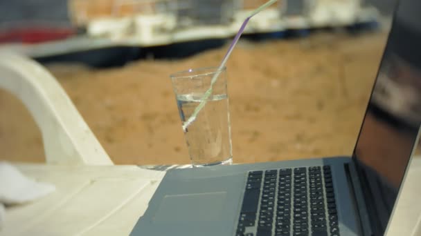 Laptop en een glas water op een chaise longue met uitzicht op de Oceaan — Stockvideo