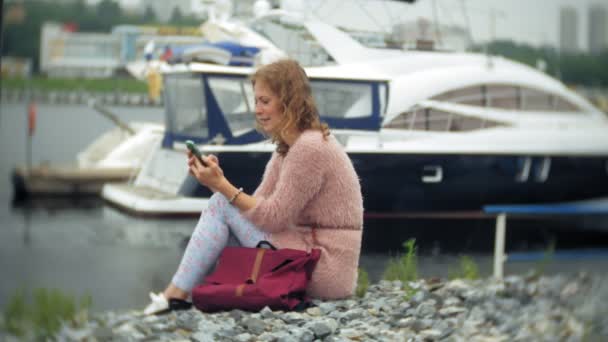 En flicka med en smartphone på seaside, yacht och segling i hamnen. — Stockvideo