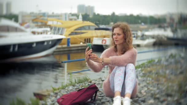 Ei jente som bruker smarttelefon ved sjøen, yacht og seiler i havnen . – stockvideo