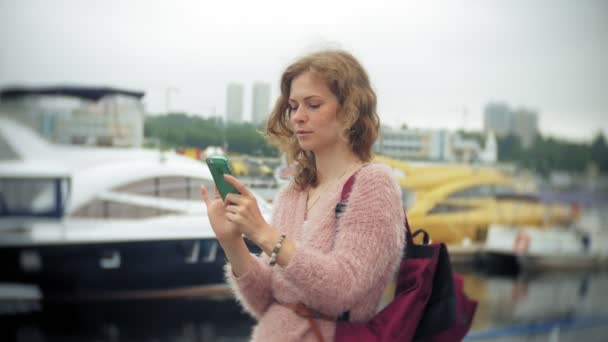 Дівчина, що використовує смартфон на узбережжі, яхт і плаває в гавані . — стокове відео