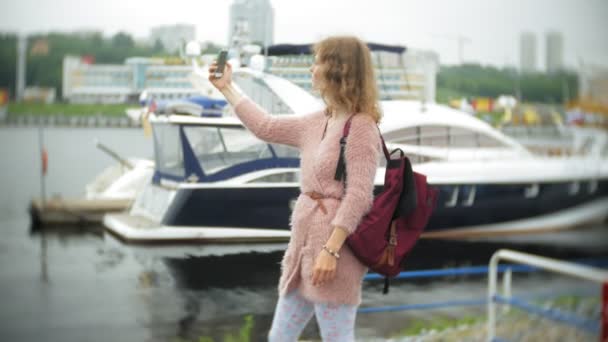 Uma menina usando um smartphone à beira-mar, iate e vela no porto . — Vídeo de Stock