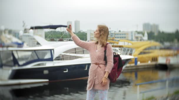 Uma menina usando um smartphone à beira-mar, iate e vela no porto . — Vídeo de Stock