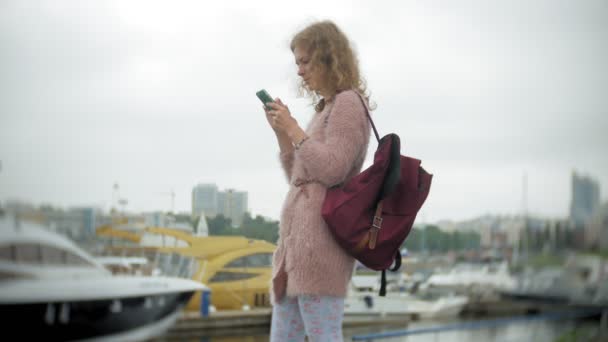 Una ragazza che utilizza uno smartphone al mare, yacht e vela nel porto . — Video Stock