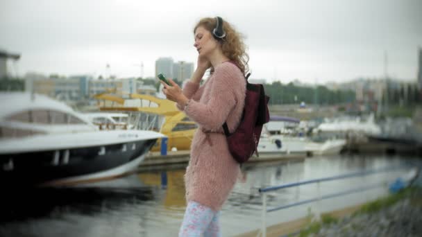 Uma menina usando um smartphone à beira-mar, iate e vela no porto . — Vídeo de Stock