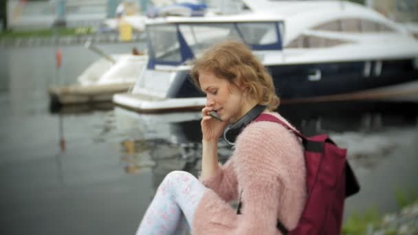 Uma menina usando um smartphone à beira-mar, iate e vela no porto . — Vídeo de Stock