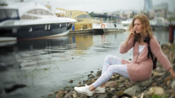 Ein Mädchen mit einem Smartphone am Strand, Musik über Kopfhörer hören, eine Jacht tanzen und im Hafen segeln. — Stockvideo