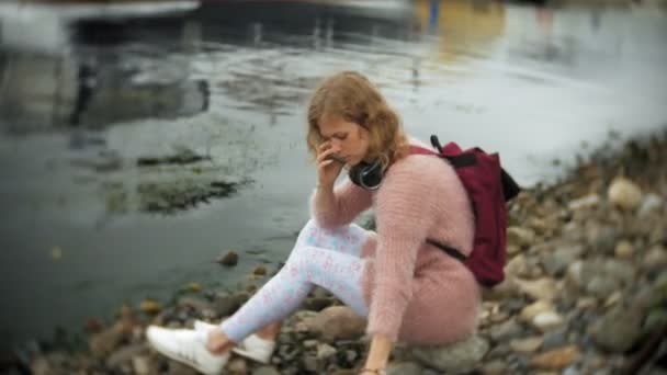 Une fille utilisant un smartphone sur la plage, écoutant de la musique dans les écouteurs, dansant un yacht et naviguant dans le port . — Video