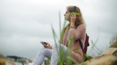 Kulaklık müzik dinlemek, bir yat dans ve limanda yelken bir smartphone sahilde, kullanan bir kız.