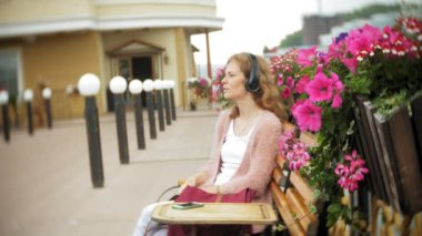 Kız çıtır sahilde, bir bankta bir smartphone kullanarak kulaklık müzik dinlemek, bir yat dans ve limanda yelken.