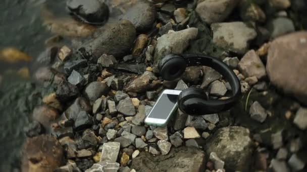 Auriculares y un teléfono inteligente tumbado en rocas cerca del mar, golpeando las olas — Vídeos de Stock