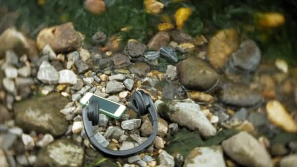 Ακουστικά και ένα smartphone που βρίσκεται στα βράχια δίπλα στη θάλασσα, ήττα κύματα — Αρχείο Βίντεο