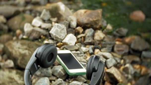Écouteurs et un smartphone couché sur des rochers près de la mer, battant les vagues — Video