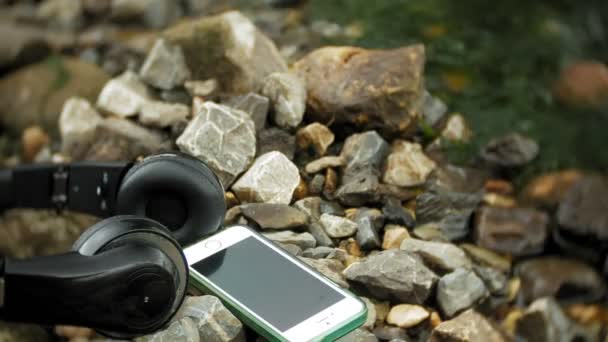 Écouteurs et un smartphone couché sur des rochers près de la mer, battant les vagues — Video