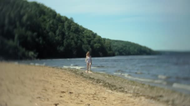 Молодая девушка в белом бикини идет вдоль берега — стоковое видео
