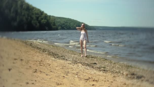 Молодая девушка в белом бикини идет вдоль берега — стоковое видео
