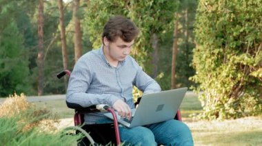Engelli biri tekerlekli sandalyede oturan ve parkta bir dizüstü bilgisayar üzerinde çalışan
