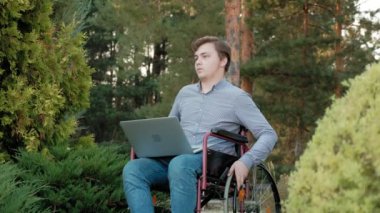 Engelli biri tekerlekli sandalyede oturan ve parkta bir dizüstü bilgisayar üzerinde çalışan