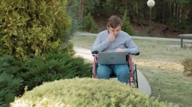 Engelli biri tekerlekli sandalyede oturan ve parkta bir dizüstü bilgisayar üzerinde çalışan