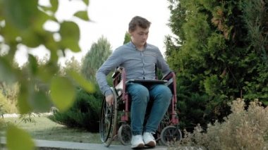 Engelli biri tekerlekli sandalyede oturan ve parkta bir dizüstü bilgisayar üzerinde çalışan