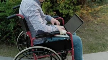 Engelli biri tekerlekli sandalyede oturan ve parkta bir dizüstü bilgisayar üzerinde çalışan