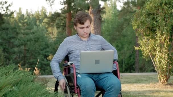 Egy fogyatékkal élő ember ült a kerekesszékben, és működő-ra egy laptop a parkban — Stock videók