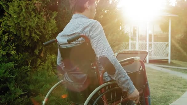 Un handicapé est assis dans un fauteuil roulant et travaille sur un ordinateur portable dans le parc — Video