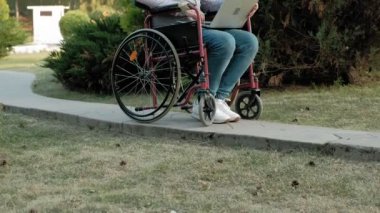 Engelli biri tekerlekli sandalyede oturan ve parkta bir dizüstü bilgisayar üzerinde çalışan