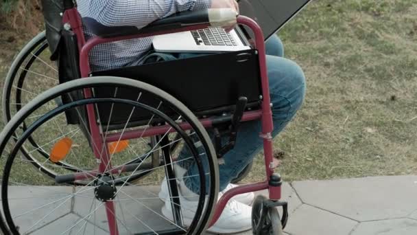 Postižený člověk sedí na vozíku a pracují na přenosném počítači v parku — Stock video
