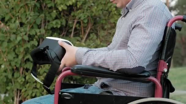 En inaktiverad man i en rullstol stol klänningar en virtuell verklighet hjälm — Stockvideo