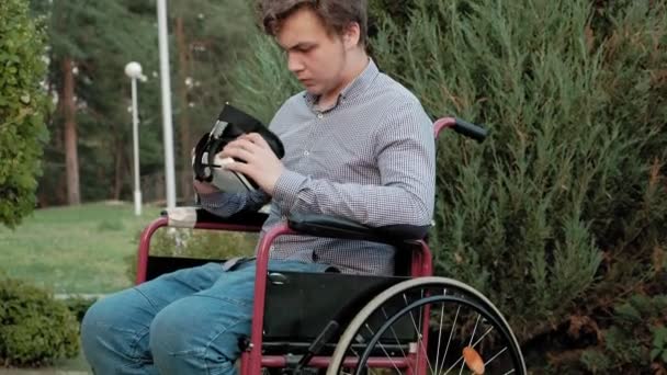 A disabled man in a wheelchair chair dresses a virtual reality helmet — Stock Video