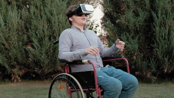 A disabled man in a wheelchair chair uses a virtual reality helmet — Stock Video