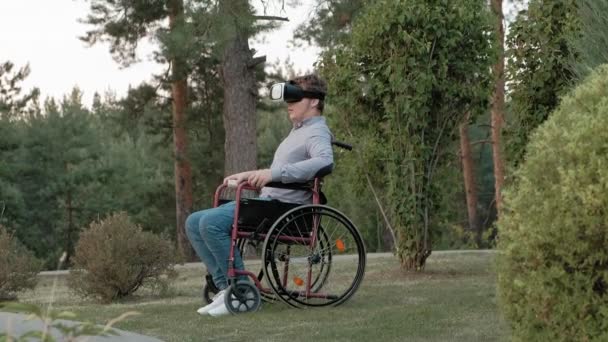 A disabled man in a wheelchair chair uses a virtual reality helmet — Stock Video