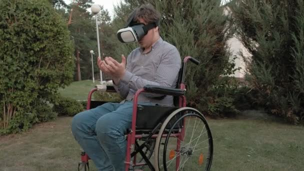 A disabled man in a wheelchair chair uses a virtual reality helmet — Stock Video