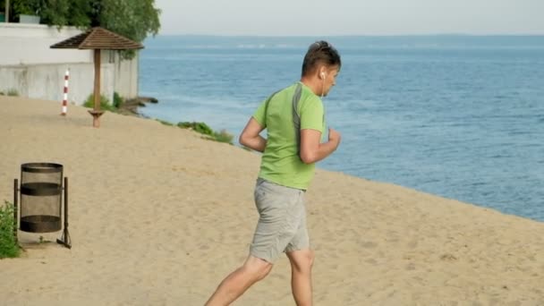 Un hombre maduro se dedica a la gimnasia en el mar al amanecer. Ella corre a lo largo de la costa en auriculares, Super cámara lenta — Vídeo de stock