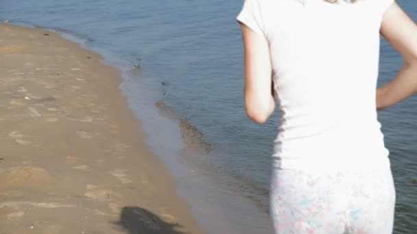 Une jeune femme avec une belle silhouette est engagée dans la gymnastique dans la mer à l'aube. Elle court le long de la côte dans les écouteurs, Super slow motion — Video