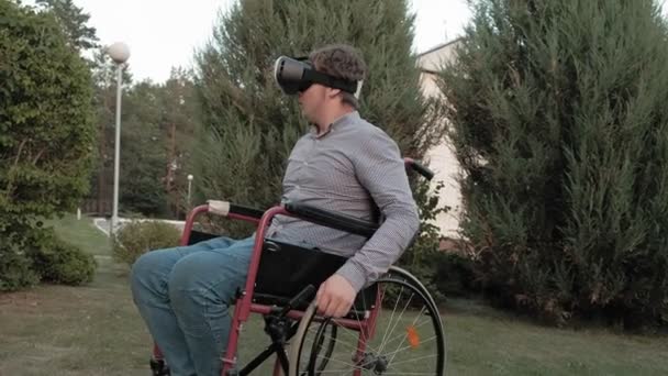 A disabled man in a wheelchair chair uses a virtual reality helmet — Stock Video