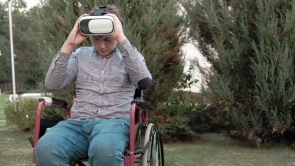 Een gehandicapte man in een rolstoel stoel verwijdert de vr-helm — Stockvideo