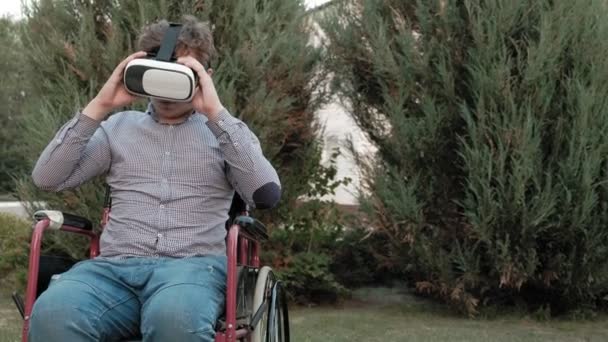 Ένα ανάπηρο άνθρωπο σε μια αναπηρική καρέκλα καρέκλα αφαιρεί το κράνος εικονικής πραγματικότητας και πετάει — Αρχείο Βίντεο