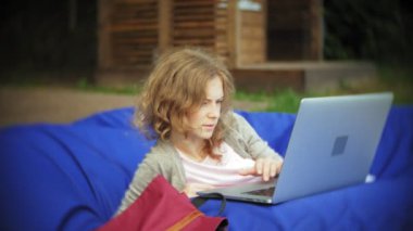 Genç kadın bir dizüstü bilgisayar, yumuşak puffs üzerinde Park lounge alanında yalan kullanır