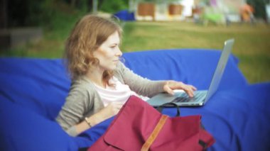 Genç kadın bir dizüstü bilgisayar, yumuşak puffs üzerinde Park lounge alanında yalan kullanır