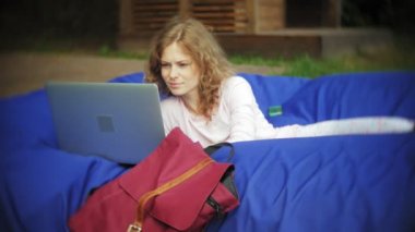 Genç kadın bir dizüstü bilgisayar, yumuşak puffs üzerinde Park lounge alanında yalan kullanır