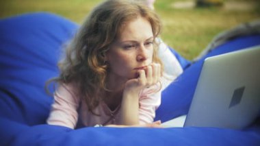 Genç kadın bir dizüstü bilgisayar, yumuşak puffs üzerinde Park lounge alanında yalan kullanır