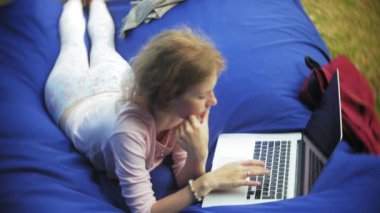 Genç kadın bir dizüstü bilgisayar, yumuşak puffs üzerinde Park lounge alanında yalan kullanır