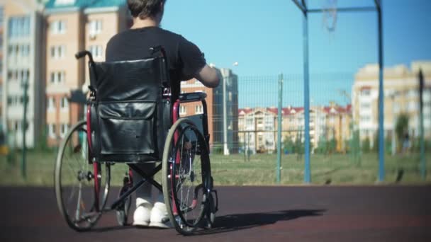 Homem com deficiência joga basquete de sua cadeira de rodas, ao ar livre — Vídeo de Stock