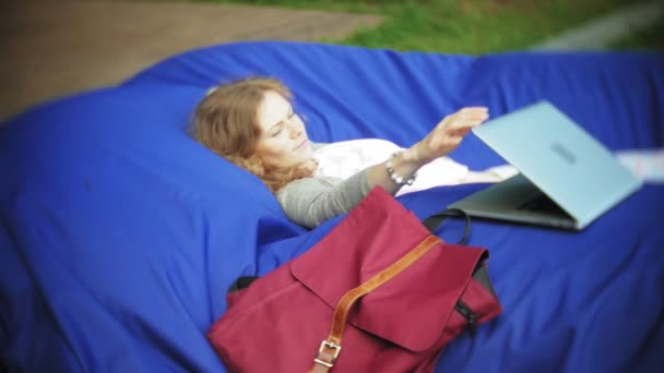 Mladá žena používá notebook, ležící v salonku parku na měkké obláčky — Stock video