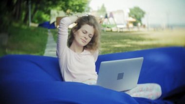Genç kadın bir dizüstü bilgisayar, yumuşak puffs üzerinde Park lounge alanında yalan kullanır