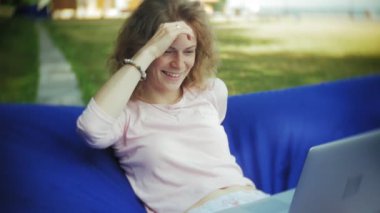 Genç kadın bir dizüstü bilgisayar, yumuşak puffs üzerinde Park lounge alanında yalan kullanır