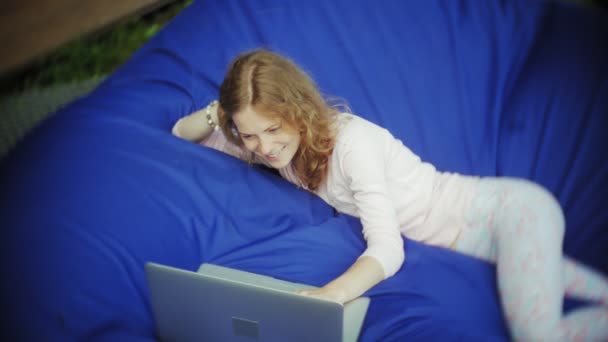 Mujer joven utiliza un ordenador portátil, acostado en una sala de estar del parque en soplos suaves — Vídeo de stock