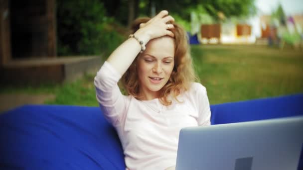 Junge Frau benutzt einen Laptop, der in einem Lounge-Bereich des Parks auf weichen Windbeutel liegt — Stockvideo