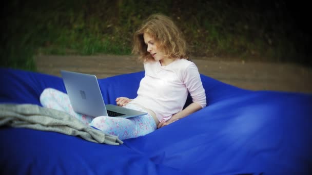 Młoda kobieta używa laptopa, leżącego w salonie parku na miękkie ciasta francuskiego — Wideo stockowe